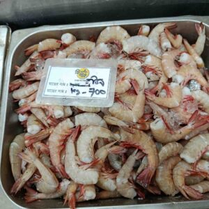 Fresh headless brown shrimp with reddish tails displayed with ice in a metal market tray at Fish Park