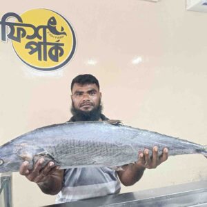 A shopkeeper holding a very large, fresh whole Surma fish horizontally at a Fish Park store, showcasing its impressive size