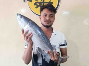 A shop attendant holding a large, freshly caught whole Tuna fish diagonally in front of a Fish Park store sign