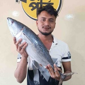A shop attendant holding a large, freshly caught whole Tuna fish diagonally in front of a Fish Park store sign