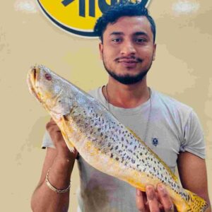 A store assistant holding a large, fresh whole premium Spot Jew fish with unique black spots and a golden hue, displayed in front of a Fish Park sign.