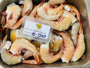Large, raw, head-on jumbo White Shrimp neatly arranged in a metal market display tray with a price placard written in Bengali.